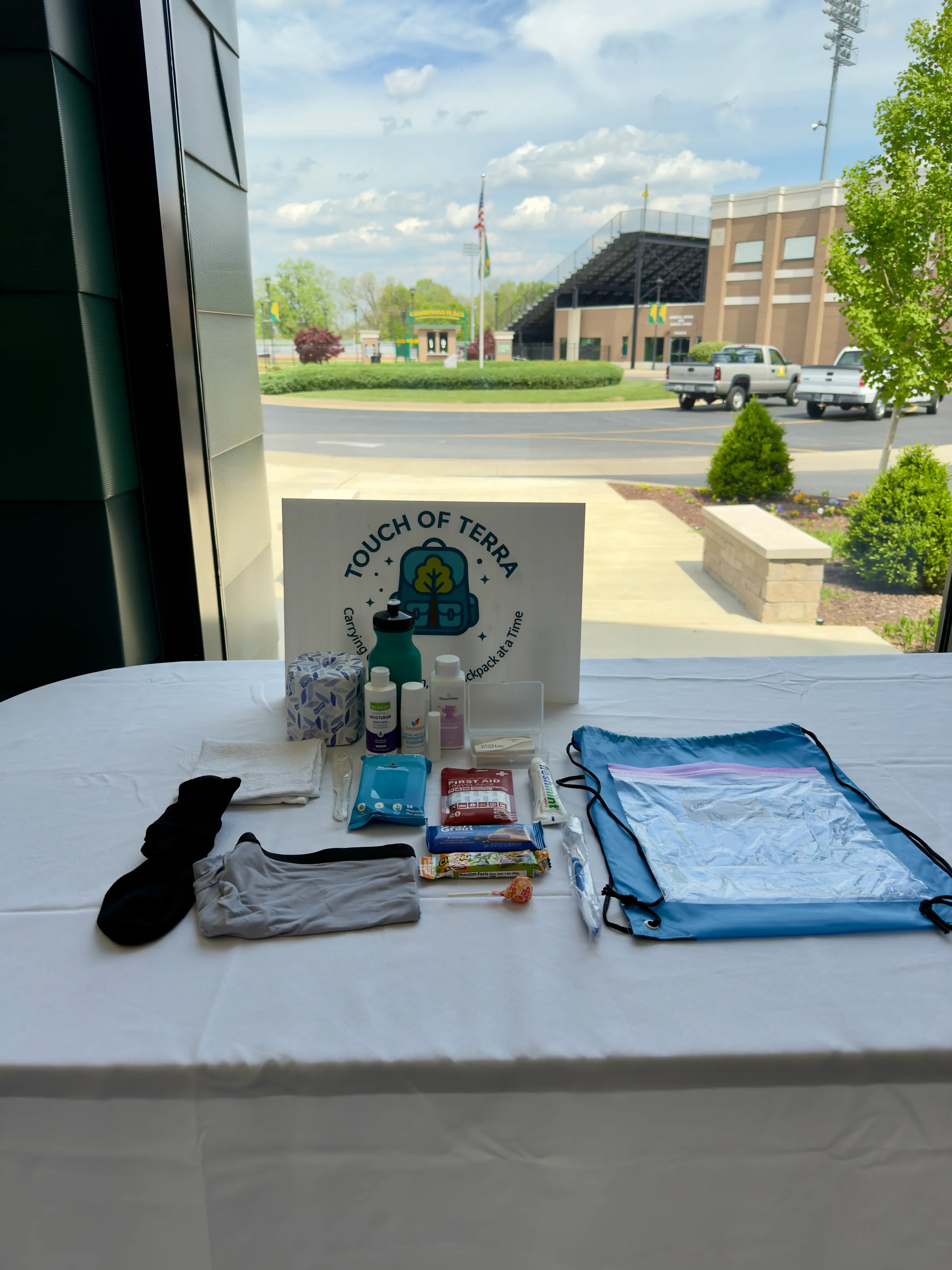 A Touch of Terra care pack and blue backpack laid out, with a high school beyond the window.
