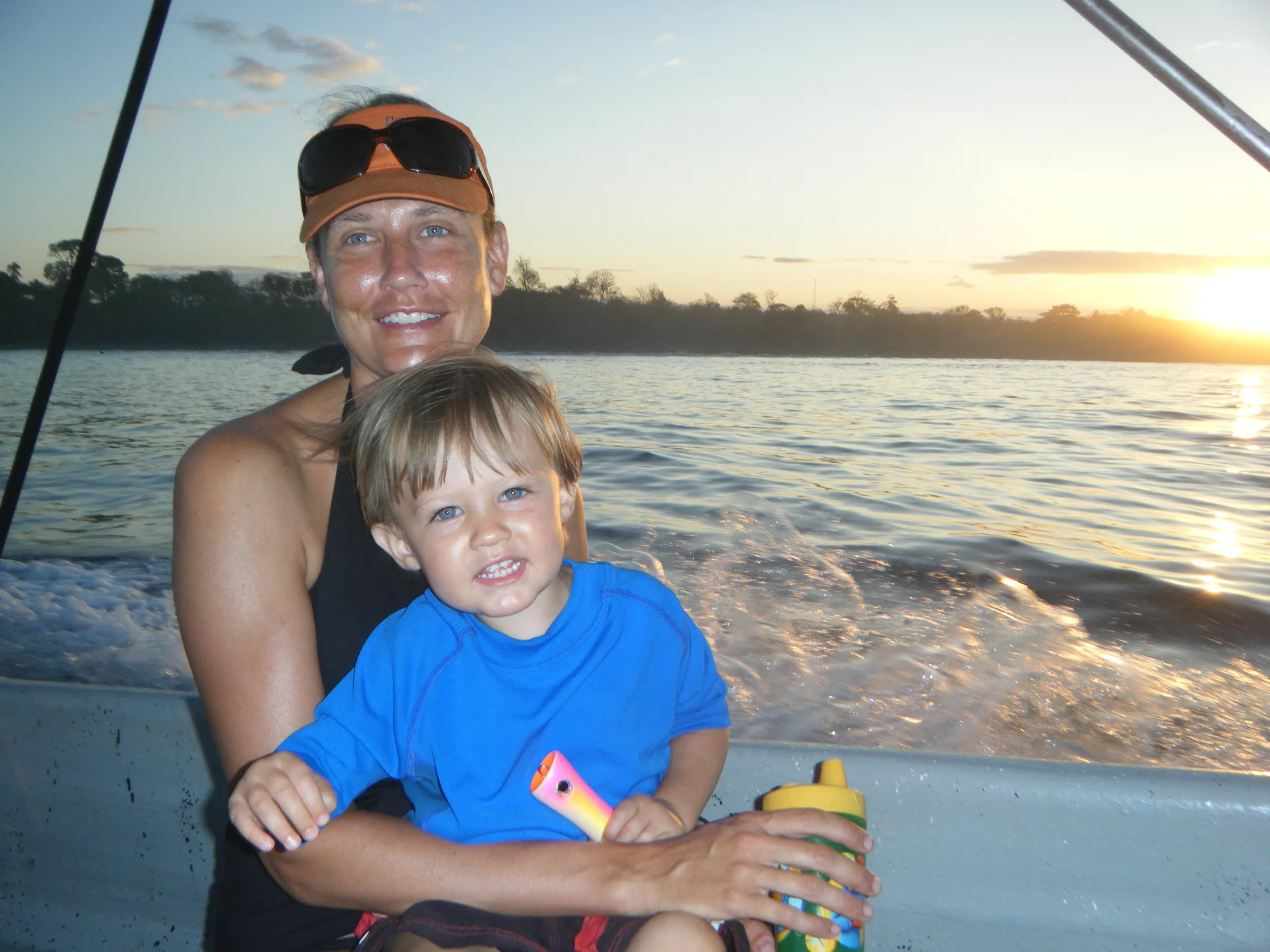 Terra Boone holding a small child on the water at sunset, both smiling.